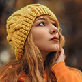 A professional close-up portrait of a student testimonial. She is wearing a yellow knit beanie and a matching yellow top, looking upward with a thoughtful and inspired expression against a soft, natural background.